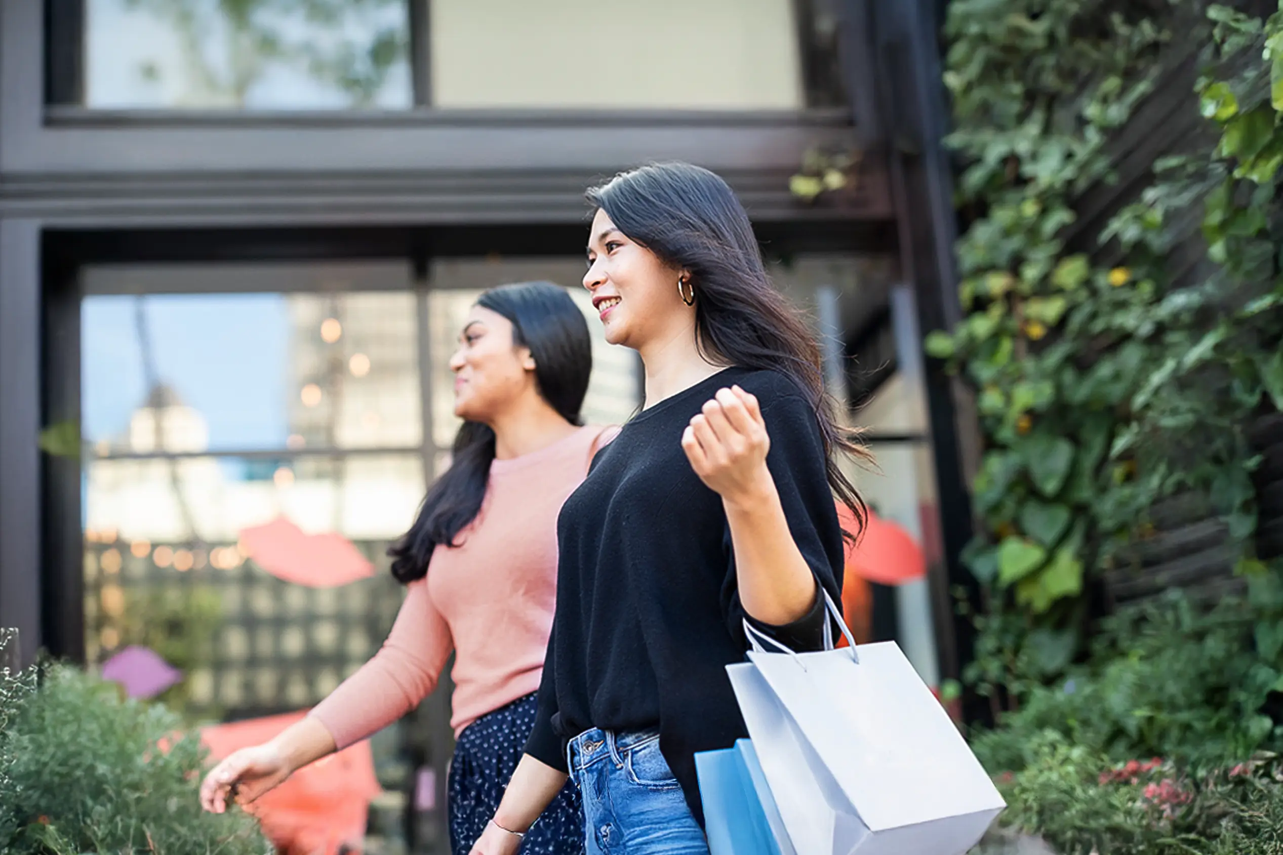 A woman happily shopping with her friend, carrying a white shopping bag.